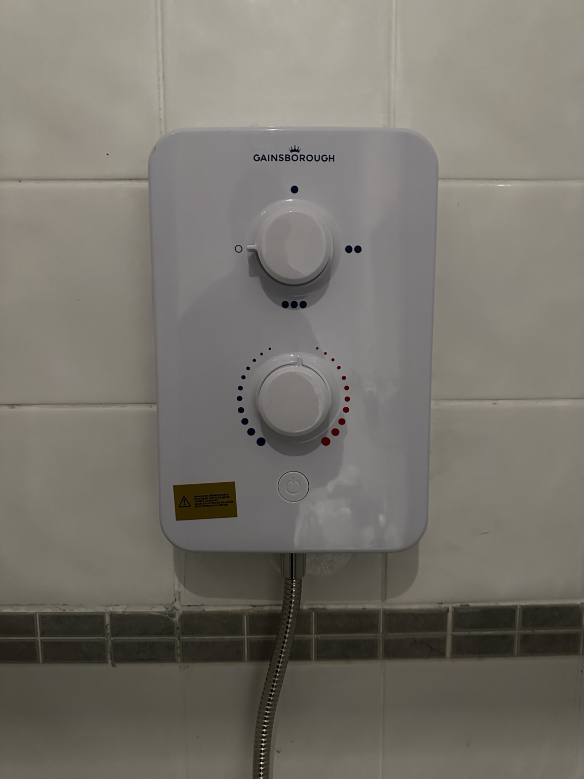 New white Gainsborough electric shower fitted against tiled wall