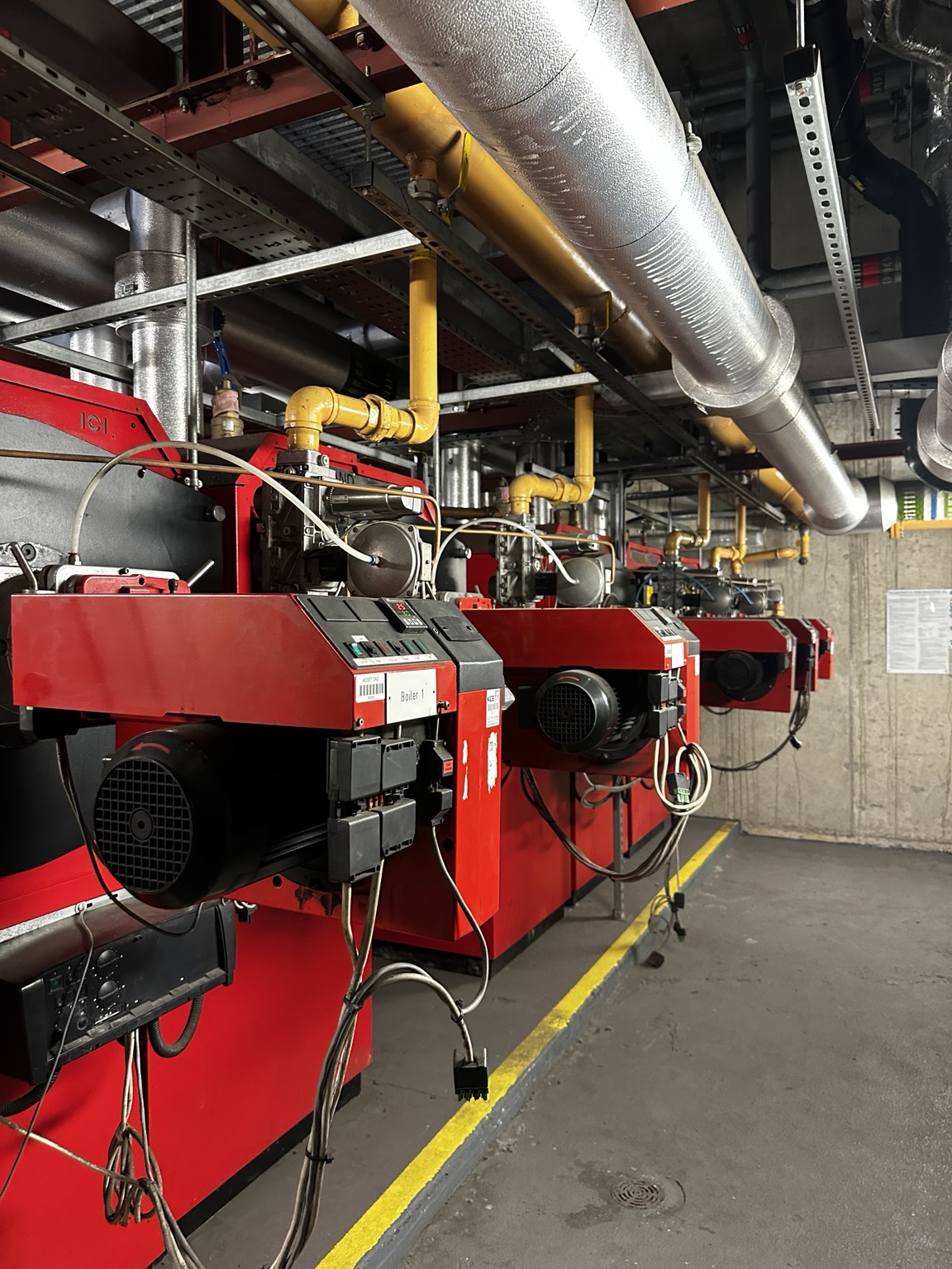 Row of red commercial boilers with gas pipework and overhead insulated services