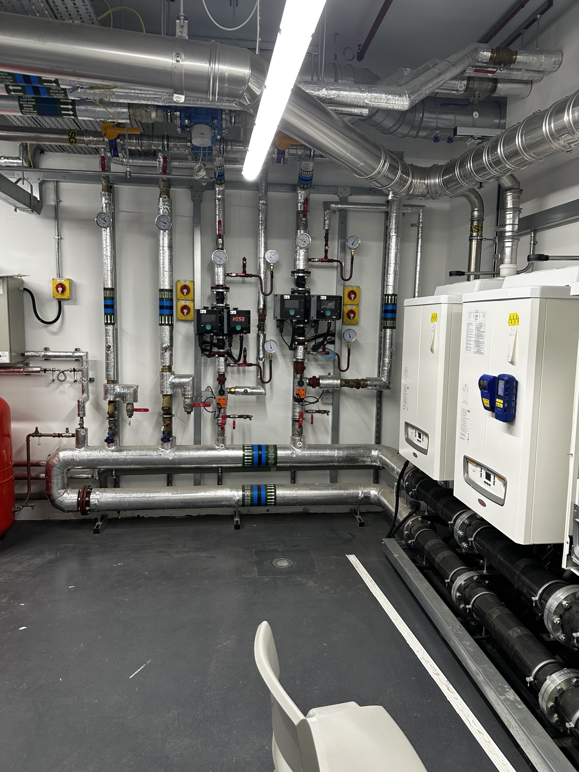 Commercial plant room with wall-mounted boilers, insulated pipework and pump groups